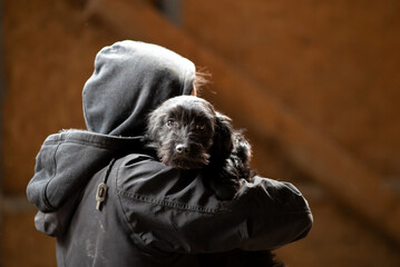 Man with hood carrying dog on shoulder