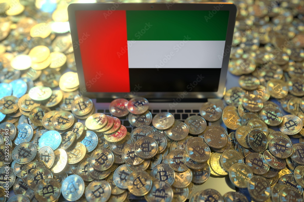 Poster computer with flag of the uae and pile of bitcoins. national regulations and cryptocurrency mining c
