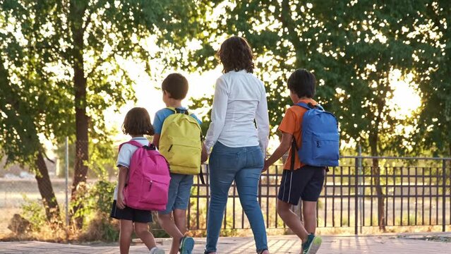 mother with her three small children holding hands walking back to school