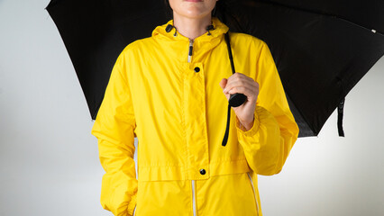 A woman in yellow raincoat holds a black umbrella on a white background © Ekaterina
