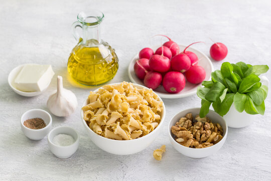 Ingredients for salad, pasta and other vegetarian dish: pasta, radish, arugula, walnuts, feta cheese, garlic, olive oil, salt and pepper on gray background. The concept of cooking vegetarian food