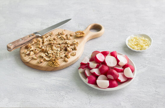 Vegetarian salad ingredients: sliced radishes, chopped walnuts, minced garlic on a light gray background. The concept of cooking vegetarian homemade food