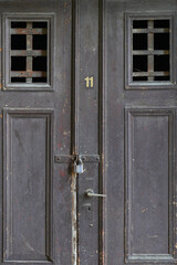 Old brown wooden door with a lock and an iron handle.Many scratches.Iron lattice.Mystery behind the lock.Retro style,vintage.Decrepit.Very old