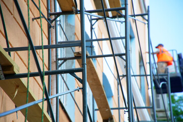 Modern wooden and metal scaffolding next to outer wall and windows of multi-storey building. Against the background of worker-plasterer in telehandler work platform. Blur and selective focus.