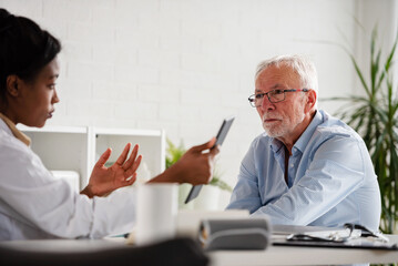 Doctor specialist consulting a patient in a doctor's office at a clinic. Female doctor is talking with a male elderly patient.