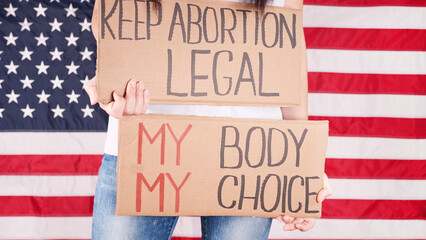 Young woman protester holds cardboard with Keep Abortion Legal and My Body My Choice signs against...