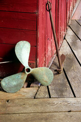 Old copper boat prop and anchor against red building © Tamela