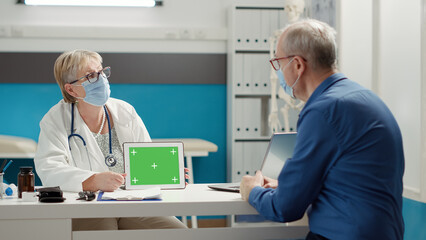 Fototapeta premium Physician holding horizontal greenscreen on digital tablet, at appointment with senior patient. Chroma key template with isolated copyspace and blank mockup background. Tripod shot.