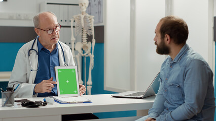 Naklejka na ściany i meble General practitioner analyzing greenscreen on device with patient in hospital cabinet. Looking at isolated chroma key template with blank mockup copyspace and background on tablet.