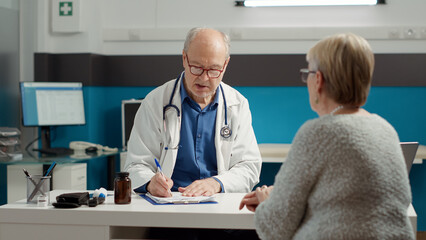 Male doctor using recovery medication to give prescription paper to retired patient in medical...