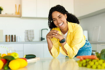 Portrait of excited african american lady posing at kitchen interior, looking at camera and smiling