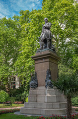 London, UK- July 4, 2022: Closeup of Sir James Outram statue in Whitehall Gardens surrounded by green foliage under small corner of blue cloudscape.  Red flowers add color.