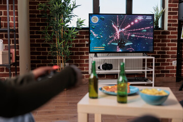 Young woman having fun with shooting video games on console, playing game competition with group of friends at house party with alcoholic drinks. People enjoying gathering with shooter strategy.