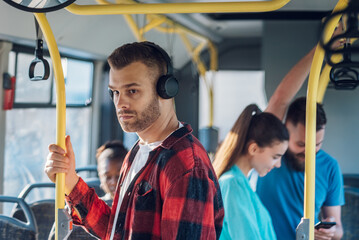 Man is riding in a bus and using headphones while holding for a bar