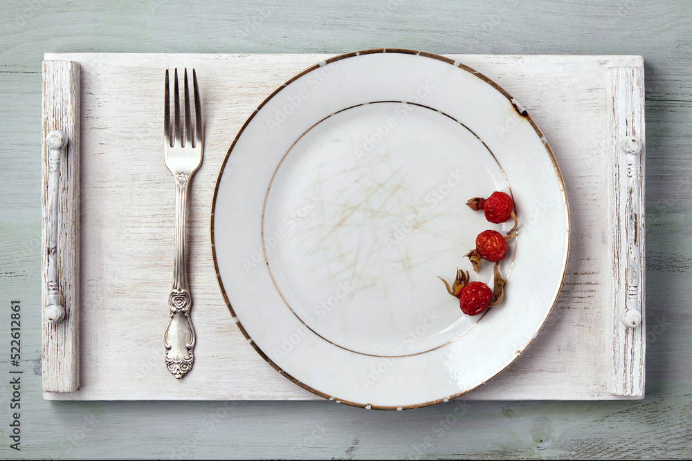 Wall mural vintage white dish garnished with rose hips with a fork on a wooden tray on a blue table. top view m