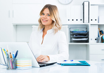 Young woman in clothes is sitting at the table in the office. High quality photo