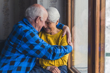 Happy loving senior family couple smiling, hugging, and touching foreheads near the window in the...