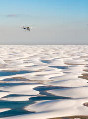 small airplane flying over white sand dunes of Lencois Maranhenses