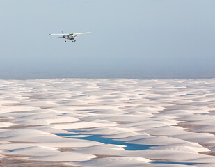 small airplane flying over white sand dunes of Lencois Maranhenses