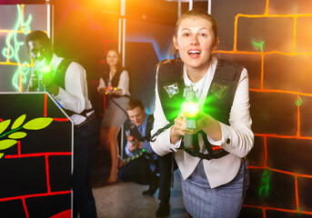 Woman in business suit holding the her laser gun and playing laser tag with colleagues