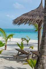 Beautiful tropical beach with white sand and two sun loungers, sun beds, on background of turquoise ocean and blue sky with clouds. Luxury resort in Maldives 2022