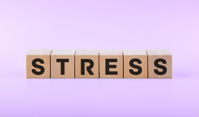 Text STRESS on wooden cubes on a pink background.
