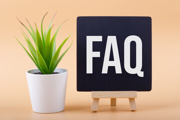 Text FAQ (Frequently Asked Questions) on a chalkboard next to a office plant on a light background. Business concept.
