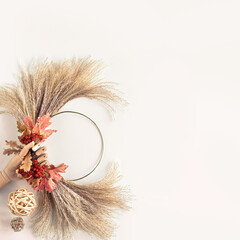 Floral wreath from dry pampas grass and Autumn leaves. Hands in sweater with manicured nails tie...