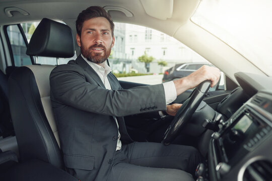 Handsome Businessman In Grey Suit Is Riding Behind Steering Wheel Of Car