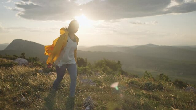 A girl tourist in a yellow jacket goes hiking along a mountain ridge. A woman traveler on a tourist trip in the mountains. High quality 4k footage