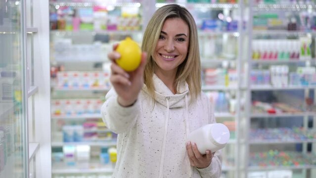 Thoughtful unsure pregnant woman choosing between pills and fruit making decision looking at camera smiling. Portrait of young beautiful Caucasian expectant stretching healthful organic lemon posing