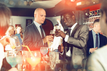 Two cheerful positive smiling male colleagues enjoying corporate bar party, drinking beer and having fun conversation