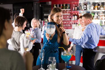 Cheerful attractive girl with cocktails having fun with workmates on corporate party at nightclub