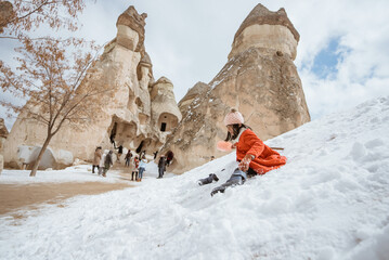 happy little girl in red sliding on a pile of snow in pasabag valley cappadocia - obrazy, fototapety, plakaty