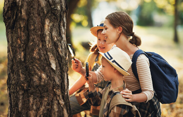 Нарру mother and two   children in   with backpacks examining tree bark through magnifying...