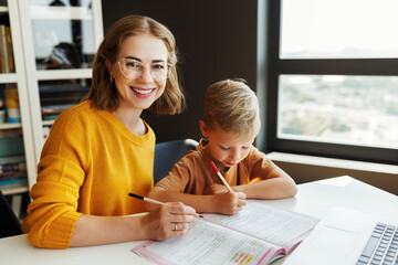 Cheerful mother doing homework with son at home - obrazy, fototapety, plakaty