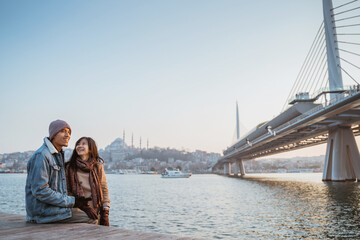 young couple relaxing on the side of bosphorus during sunset. beautiful woman and man with istanbul...