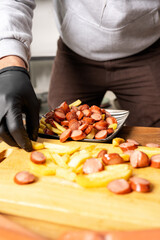 Vertical photo of a man mixing fries with sausages in a kitchen