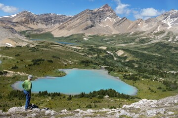 Isolated Hiker Enjoying Alpine Landscape View with Teal Colored Lake and Rocky Mountain Peaks Skyline. 
Sunny Day Scenic Summertime Hiking Banff National Park, Canadian Rockies