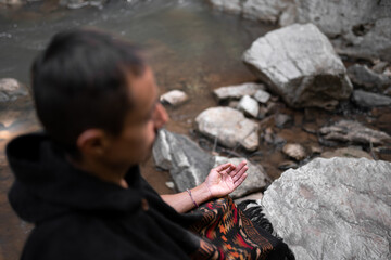 Young man meditating by the river wearing a poncho