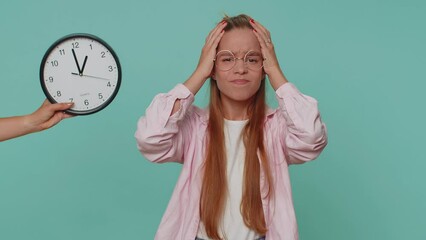 Teenager young girl with anxiety checking time on clock, running late to work, being in delay, deadline. Student child kid looking at hour, minutes, worrying to be punctual on blue studio background