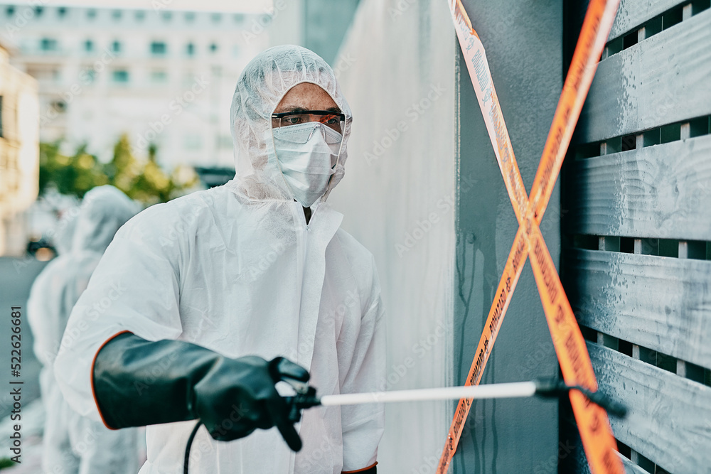 Canvas Prints Healthcare worker in covid pandemic, sanitizing and cleaning area with disinfectant, barrier or caution tape and a face mask. Emergency medical person in hazmat suit working in coronavirus crisis