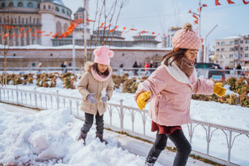 two little girl playing with snow in city square with the mosque in the background