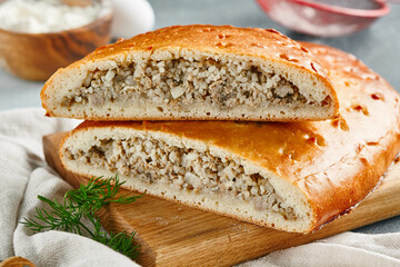 Classic pie with minced meat and rice on wooden board. Composition with meat pie on concrete background with textile and spices. Homemade pie with meat and rice in rustic style on gray table.