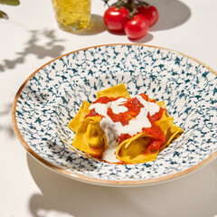 Italian ravioli with spinach, cheese and tomato in ceramic plate on white table. Cheese ravioli with creamy espuma and tomato. Italian ravioli with spinach and cheese filled and creamy topped.