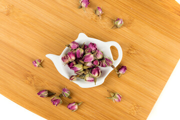 Dehydrated pink rose buds in a tea plate on a cutting board