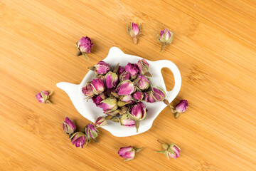 Dehydrated pink rose buds in a tea plate on a cutting board top down view