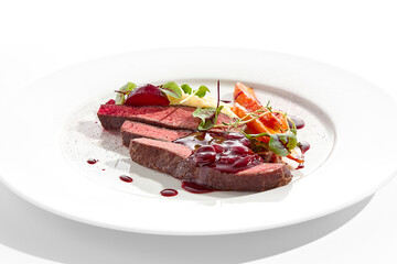 Venison steak with baked vegetables isolated on white plate. Meat steak medium rare roasted with carrot, beetroot and mashed potatoes with cherry sauce. Wild meat in restaurant menu.