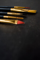Different golden make-up brushes on black background