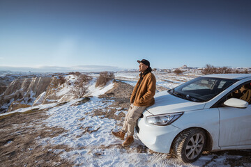 portrait of a man enjoying the view of cappadocia in winter sitting at the front of his car